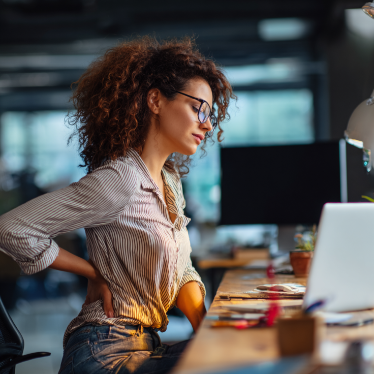 luxgrand84_a_woman_at_a_work_desk_holding_her_lower_back_in_pai_f5a5c300-ace5-44be-9f2f-0ea54cdd713b